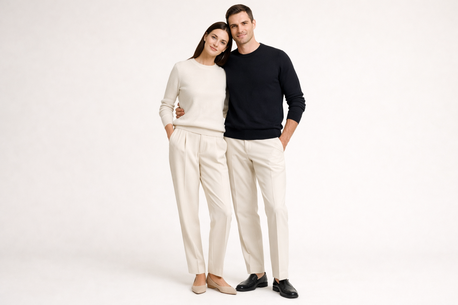 Un homme et une femme se tenant par les hanches posent pour une photo avec un fond unis. Ils portent tout deux le pull Boshu Merino de la marque HIKARI, l'homme porte la couleur noir encre et la femme la couleur ivoire.